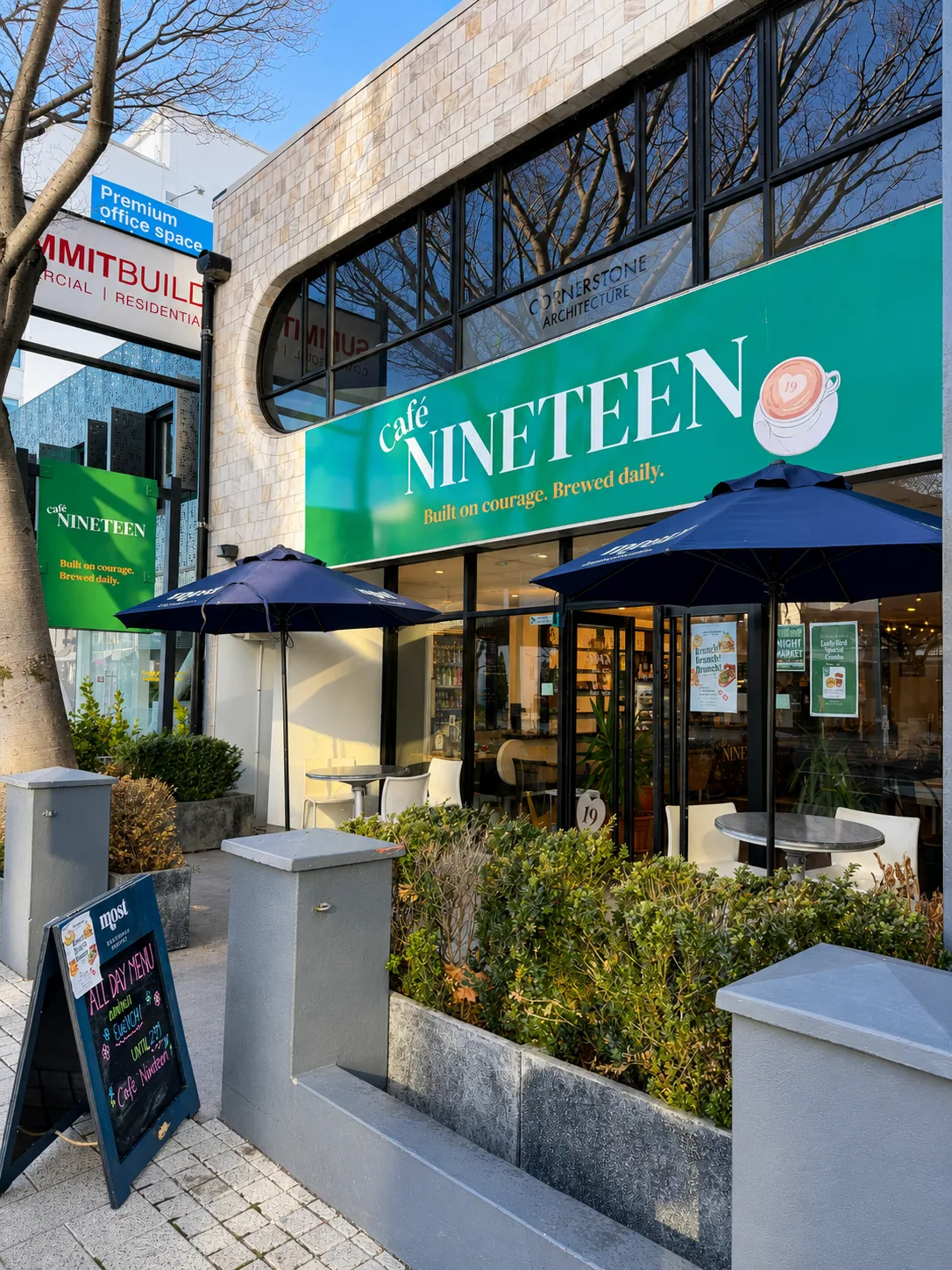 The Cafe Nineteen storefront on Victoria Street with its green sign and outdoor umbrellas