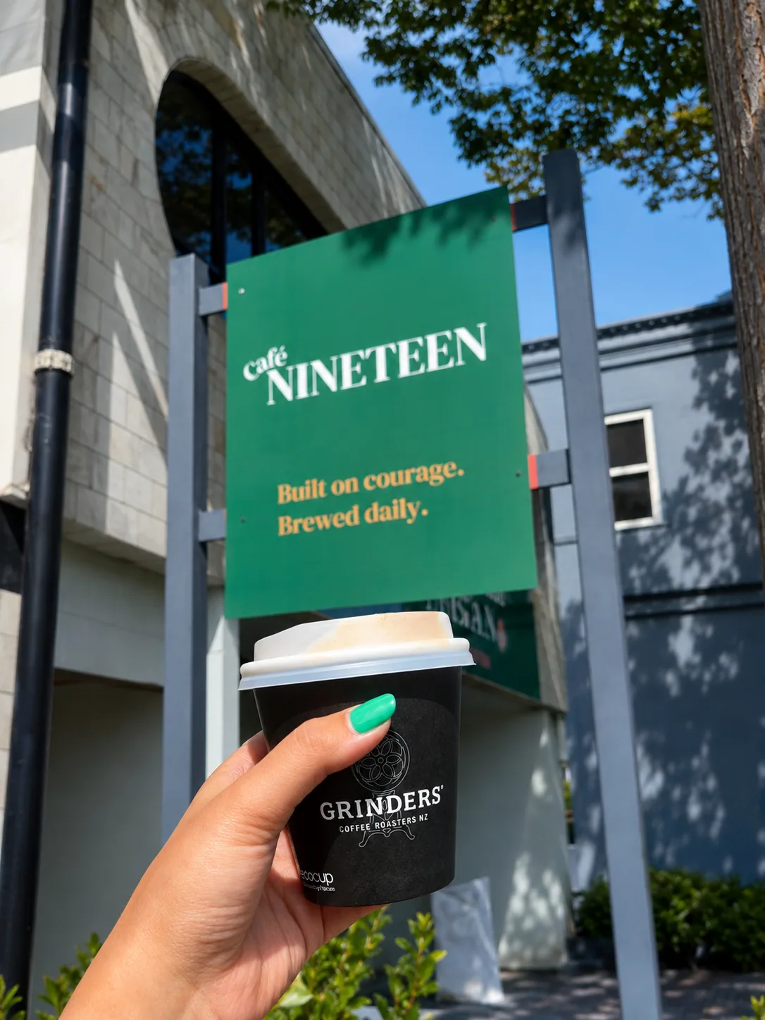 A takeaway coffee held in front of the Cafe Nineteen sign